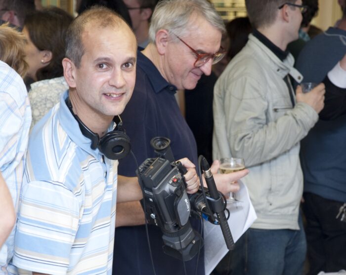 Neil Grant in a blue striped shirt, holding a video camera