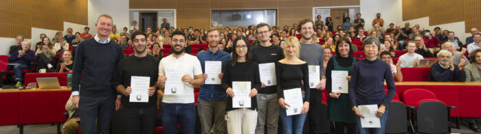 LMB prize winners with certificates in the Max Perutz Lecture Theatre with clapping audience