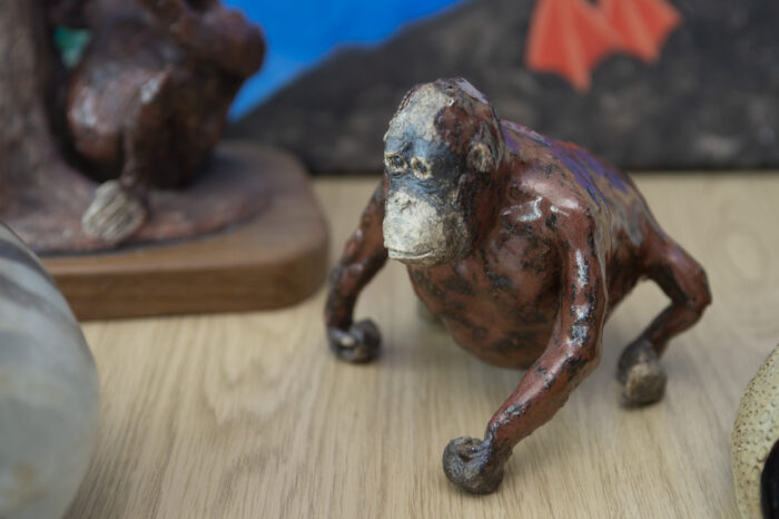 Image of a small statuette model of an orangutang placed on a table. Other models are partially visible in the background out of focus.