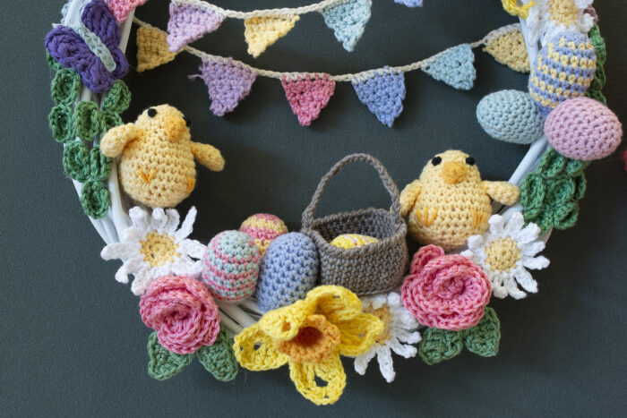 A view of half of a crocheted wreath. The design includes two chicks, eggs, a basket, flowers and bunting which crosses the circle wreath.