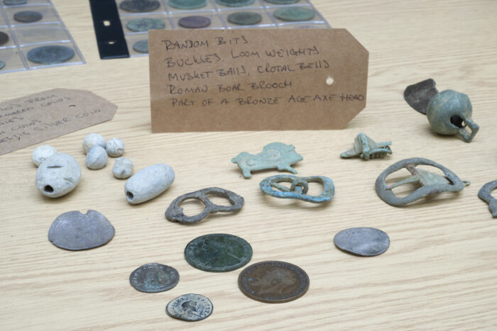 Various items found through metal detecting are displayed on a table. They include coins, brooches, buckles and loom weights. 