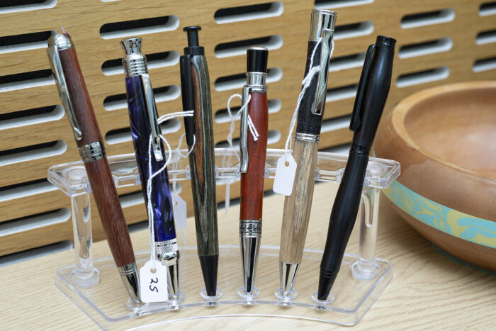 Six hand-made pens created via wood-turning displayed on a stand. 