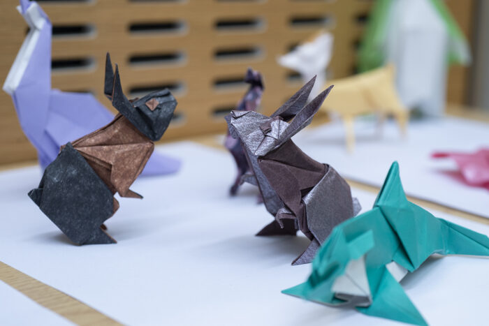 Origami rabbits in navy, brown and purple paper. An origami whale is visible out of focus in the foreground in turquoise paper.