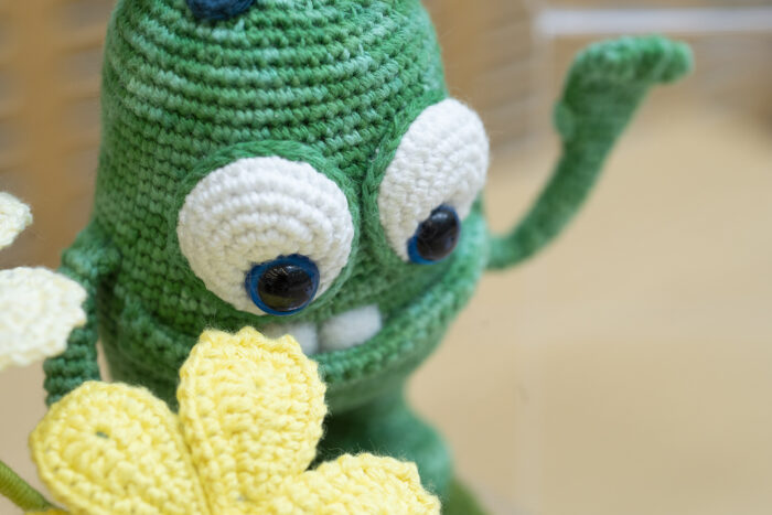 A close up of a green crocheted creature waving. 