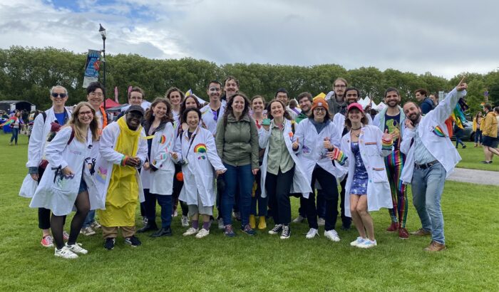 A group of people wearing smiling and waving, wearing lab coats decorated with rainbows