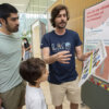 Volunteer explaining proteins scale to a father and son